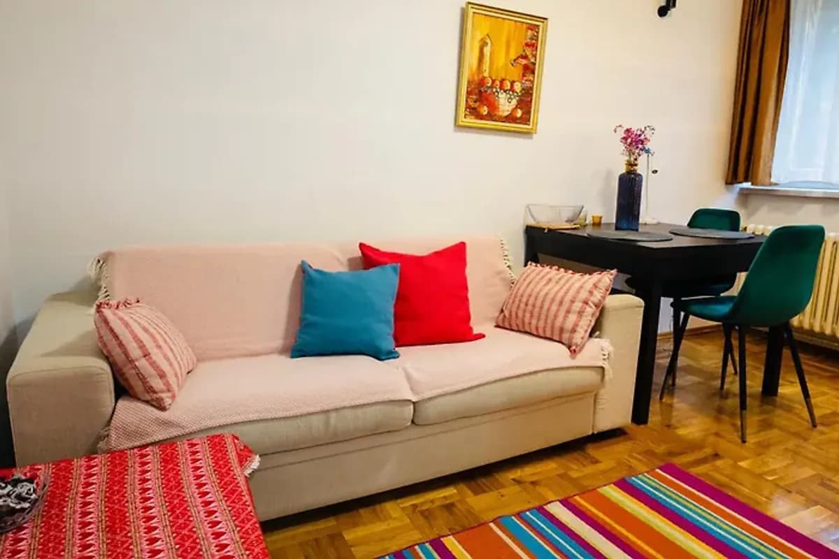 Apartman Olivia living room with beige sofa, patterned cushions, dining table and window