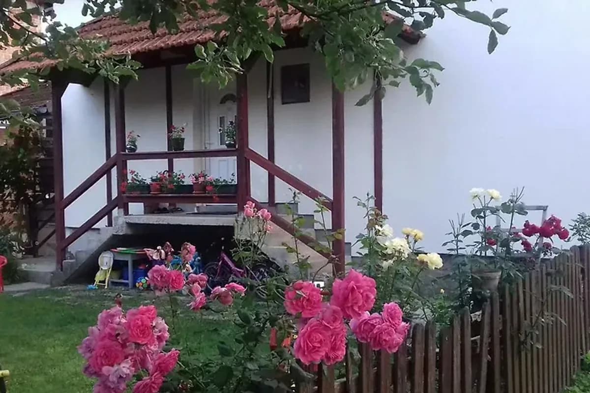 Apartment Dil Kulen Vakuf house entrance with wooden porch, pink flowers and green garden