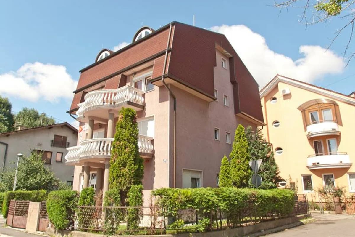 Multi-storey brown and pink hostel building with balconies and landscaped hedge at Hostel Cuba, Banja Luka