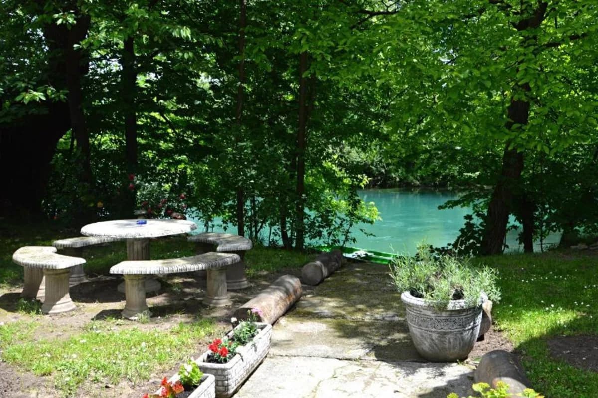 Una Rosa Hostel furnished riverside garden patio, with picnic seating beneath trees beside the Una River